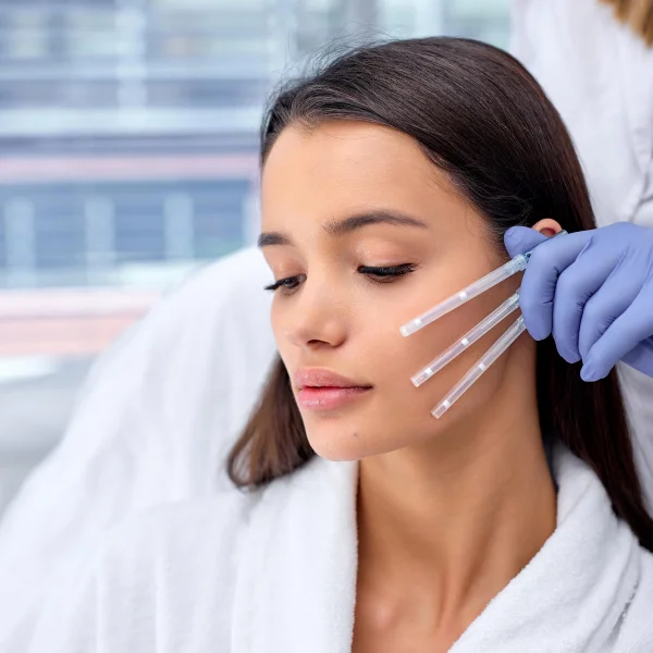 Une femme reçoit une injection au visage avec une aiguille, illustrant un traitement esthétique.