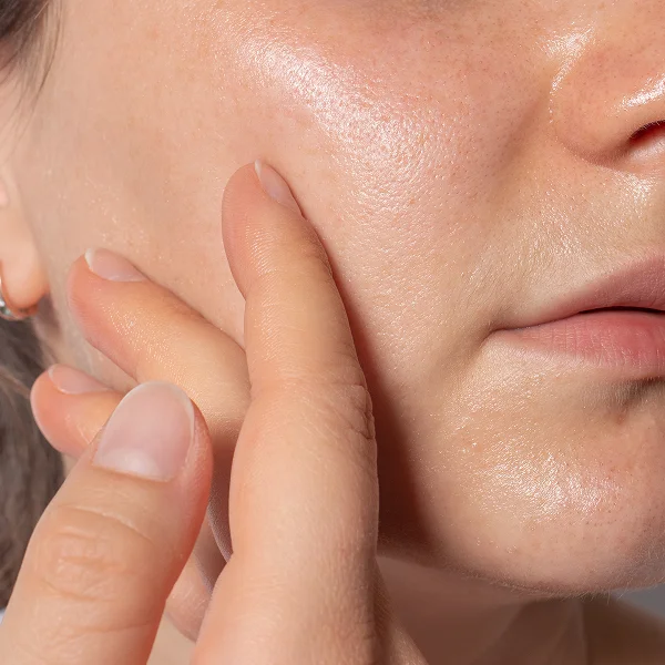 Une femme touche son visage avec ses doigts, mettant en valeur son maquillage permanent des sourcils.