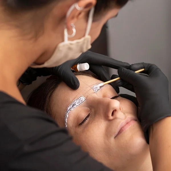 Une femme se fait faire les sourcils par un professionnel en micropigmentation.