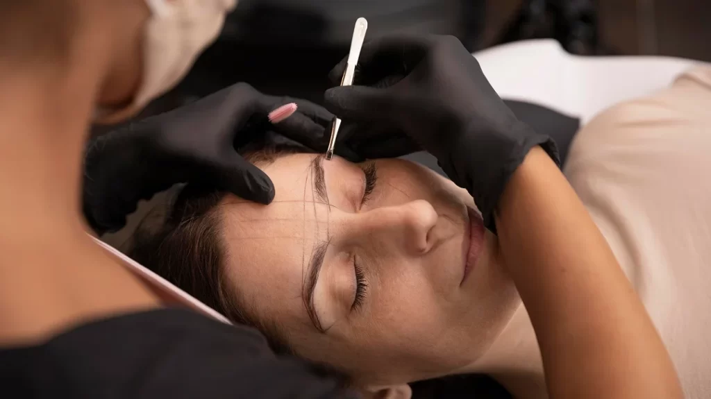 Une femme se fait faire les sourcils par un professionnel en micropigmentation.